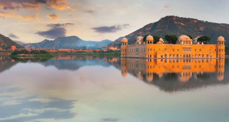 Jal Mahal water palace reflecting in serene lake at dawn with hills behind.