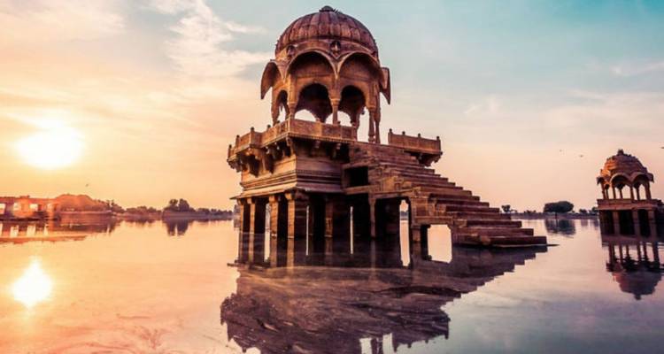 Elegant sandstone chhatri pavilion rising from tranquil lake at vibrant sunrise in Jaisalmer.
