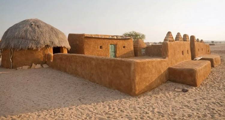 Traditional mud-plastered desert homestead with thatched roof huts under soft evening light.