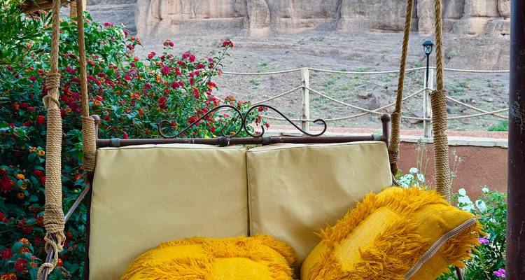 Une balançoire de jardin confortable avec des coussins jaune vif installée parmi des fleurs en fleurs et des falaises rocheuses du désert.