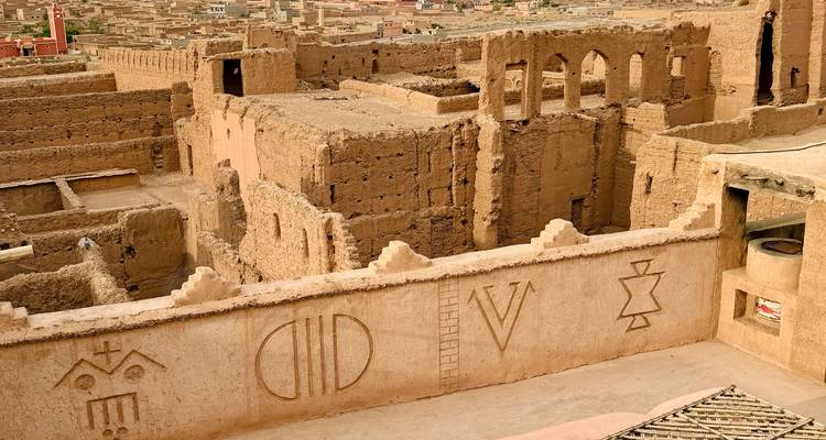 Vue élevée d'une ancienne forteresse en adobe avec des symboles gravés et des toits de ville au loin.