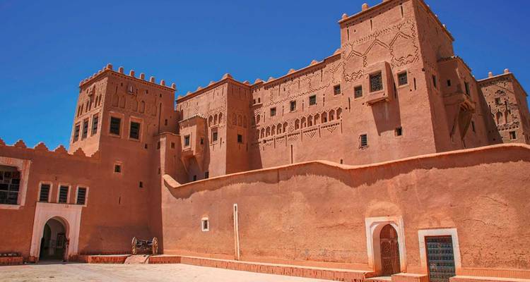 Impresionantes muros de adobe y torres de la Kasbah Taourirt bajo un cielo azul vívido.