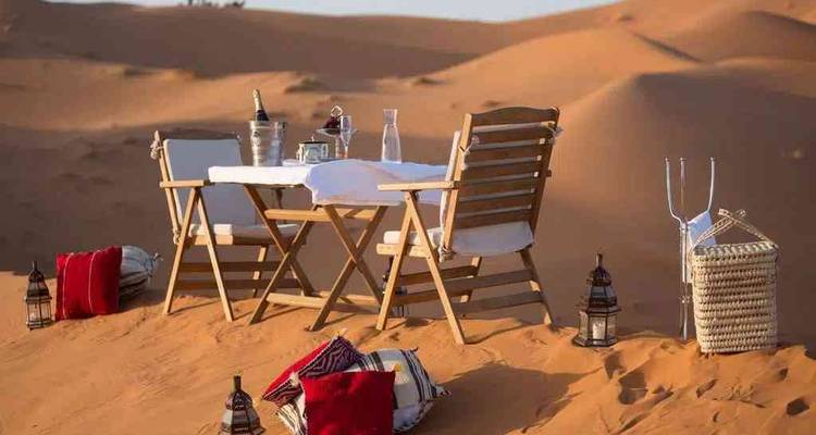 Mesa romántica puesta para dos en la cima de una duna silenciosa, rodeada de faroles.