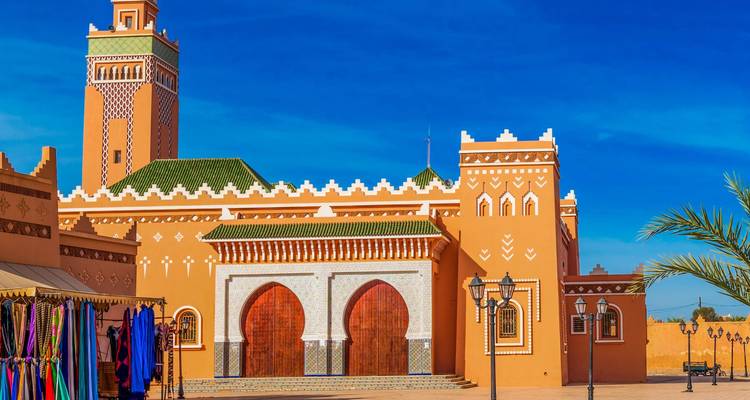 Mezquita ocre ornamentada con techo de tejas verdes y puertas gemelas arqueadas bajo un cielo azul vívido
