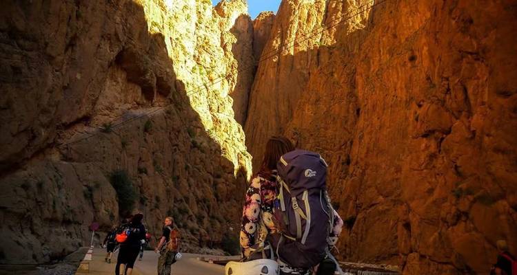 Mochileros caminan por el estrecho suelo del cañón de las Gargantas del Todra bañado en luz cálida