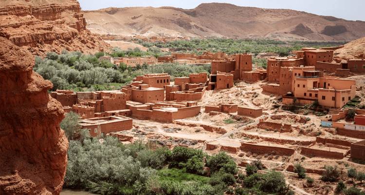 Adobe hillside village set in a lush green valley beneath arid mountains.
