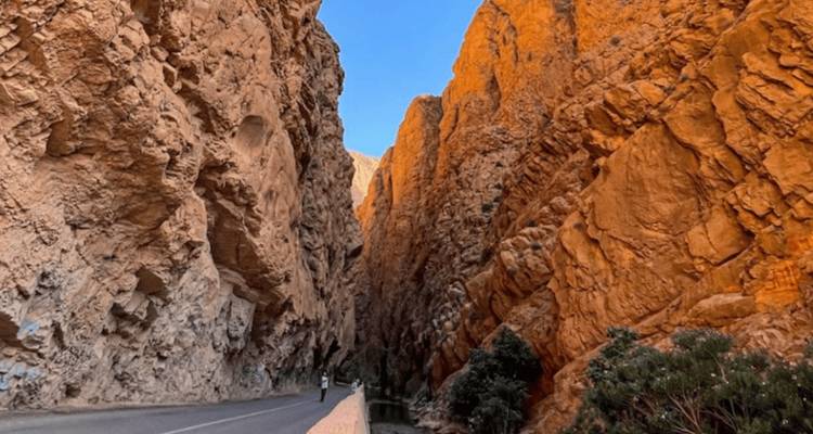 Dramatic narrow canyon with towering orange cliffs and a single roadway.