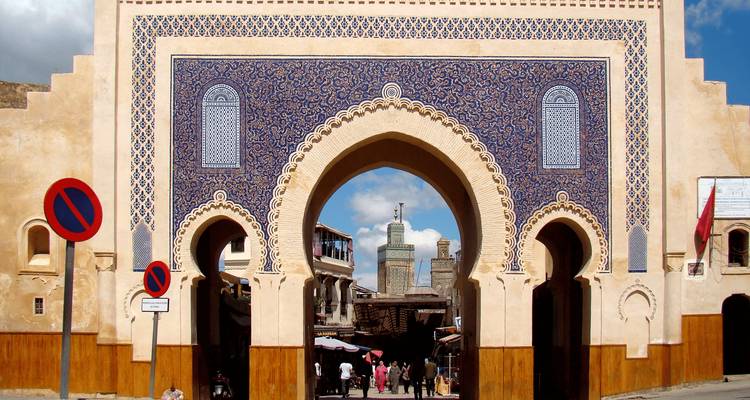 Ornate blue-tiled gate with people walking through its grand archways.