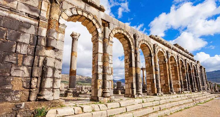 Ancient stone arches and columns of Roman ruins against a blue sky.