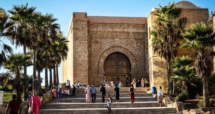 Large carved stone gate with palm trees and visitors climbing broad steps.