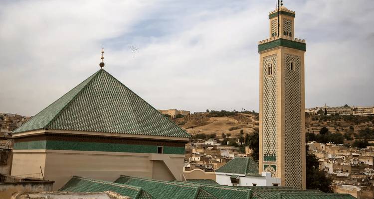 Green-tiled mosque roof and slender minaret overlooking Fes medina.