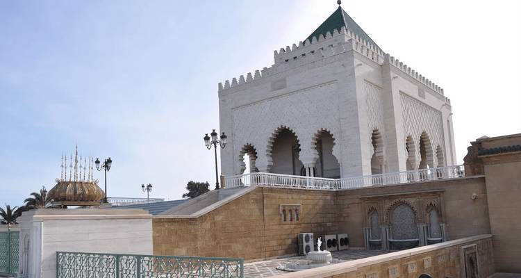 White marble Mausoleum of Mohammed V with intricate arches and green roof.