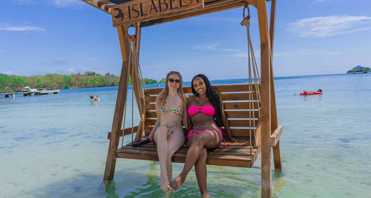 Deux femmes en bikinis colorés se détendent sur une balançoire en bois flottant au-dessus des eaux peu profondes et cristallines des Caraïbes à Isla Bela.