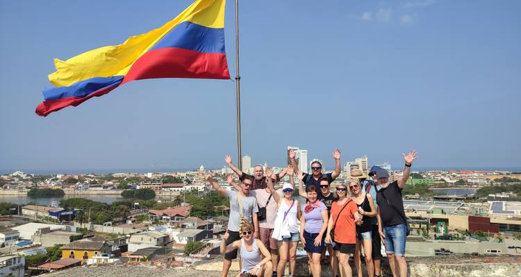 Un groupe de touristes joyeux agite les mains à côté d'un immense drapeau colombien dominant les toits de Carthagène.