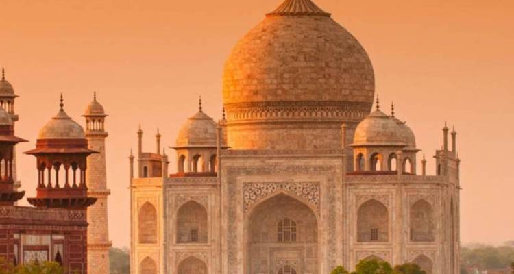 Iconic marble domes and minarets of the Taj Mahal glow warmly in soft sunset light.
