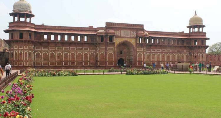Expansive courtyard with flower beds in front of the red sandstone Agra Fort palace buildings.