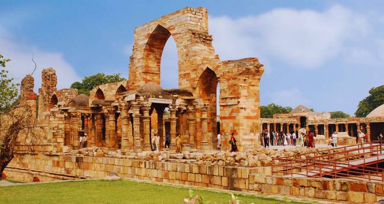 Ruined sandstone arches and columns of the ancient Quwwat complex with visitors exploring.