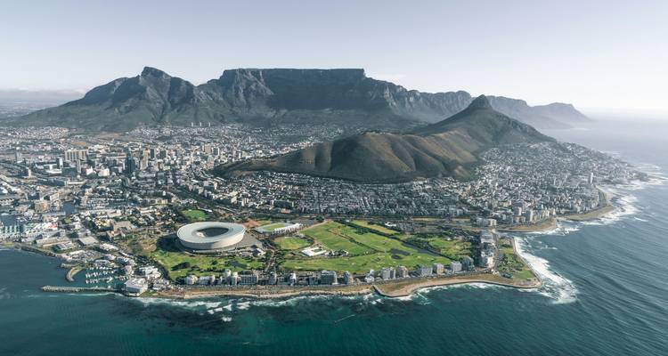 Panoramic aerial of Cape Town: Table Mountain, Lion’s Head and cityscape beside coastline.