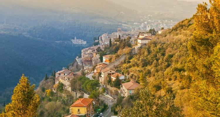 Sunlit hill town with terracotta rooftops cascades down a green valley at golden hour.