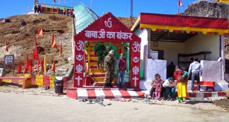 Visitors gather outside a brightly painted Himalayan shrine festooned with red flags.