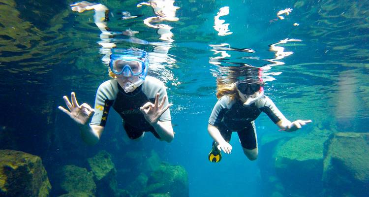 Deux plongeurs avec tuba sous l'eau font des signes OK au milieu d'un paysage de fond marin rocheux.