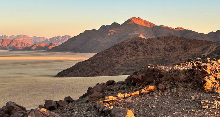 Rocky ridges and sun-tinted mountains overlooking a vast sandy plain at dawn in Namibia.