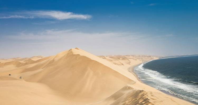Sweeping golden sand dunes meet the deep blue Atlantic coastline under a clear sky.