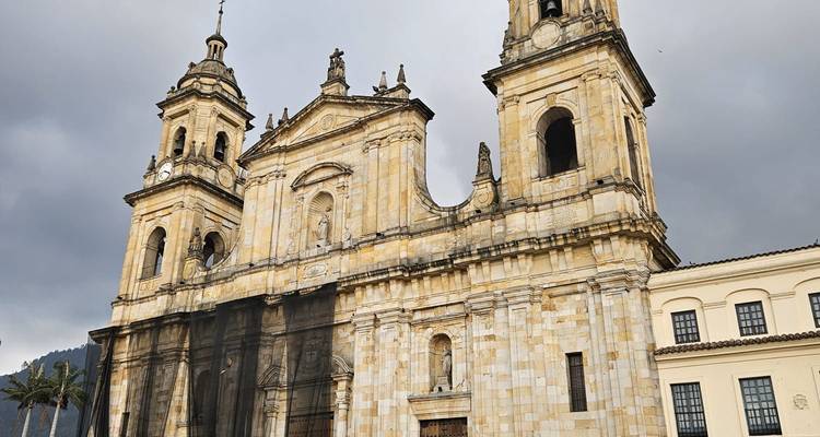 Façade en pierre de la Catedral Primada de Bogotá avec ses deux clochers jumeaux s'élevant contre un ciel gris menaçant.