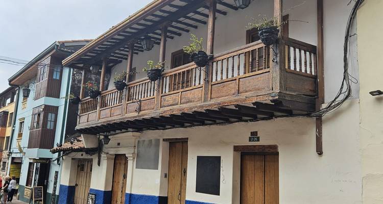 Maison coloniale traditionnelle avec balcon en bois, fleurs en pots et murs inférieurs peints en bleu et blanc sur une rue étroite de Bogotá.