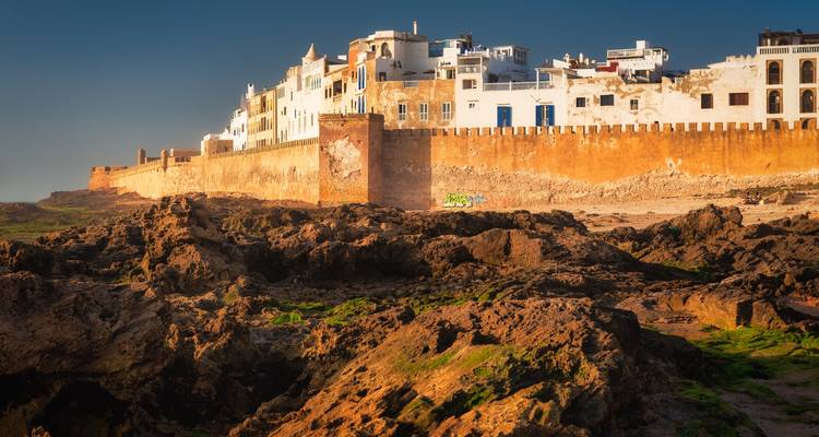 Goldene Bollwerke und weiß getünchte Häuser der Medina von Essaouira erheben sich über schroffe Küstenfelsen im warmen Nachmittagslicht.