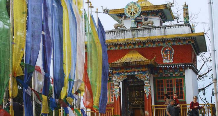 Colorful prayer flags fluttering beside a small hilltop monastery with visitors at the entrance