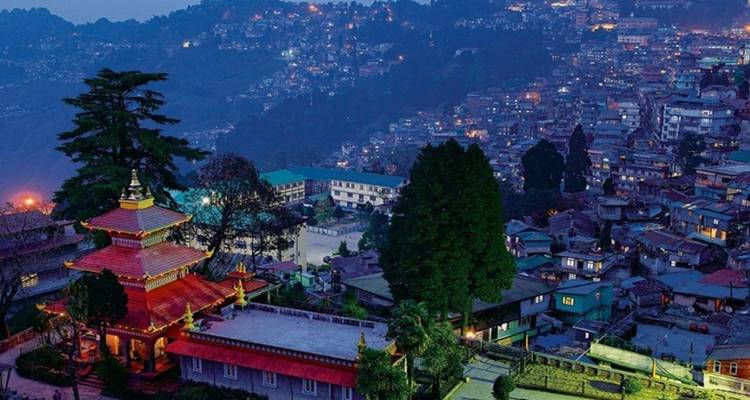 Nighttime panorama of a hillside city glowing with lights beside a lit monastery