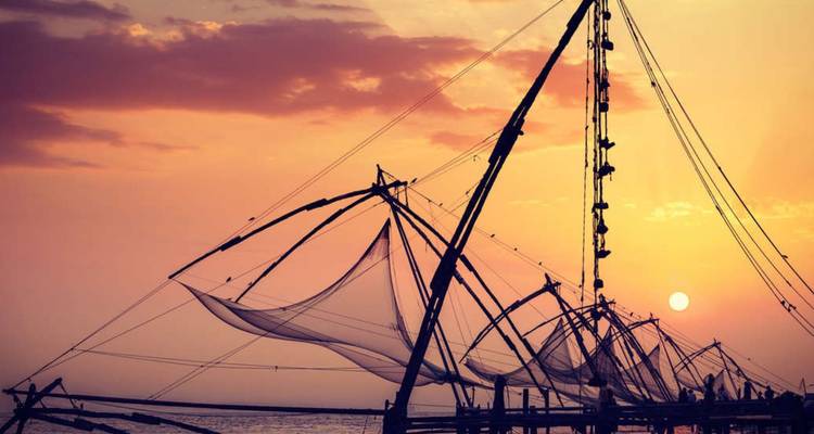 Traditional Chinese fishing nets are silhouetted against a vibrant sunset sky over the Arabian Sea.