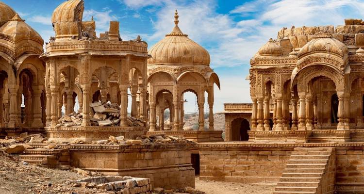 Ornate sandstone cenotaphs of Bada Bagh stand against a bright blue sky littered with clouds.