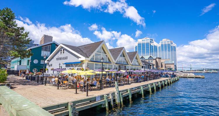 Vibrant waterfront boardwalk lined with restaurants and umbrellas on a sunny day in Halifax harbour.