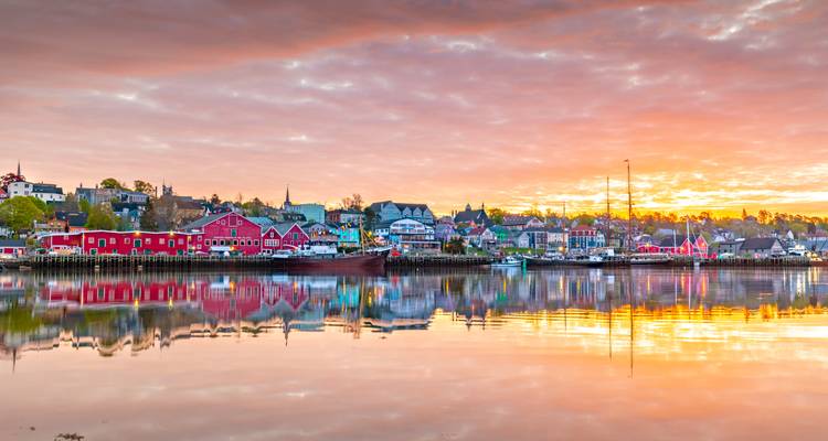 Colorful heritage buildings of Lunenburg reflected in calm harbour waters at sunrise.