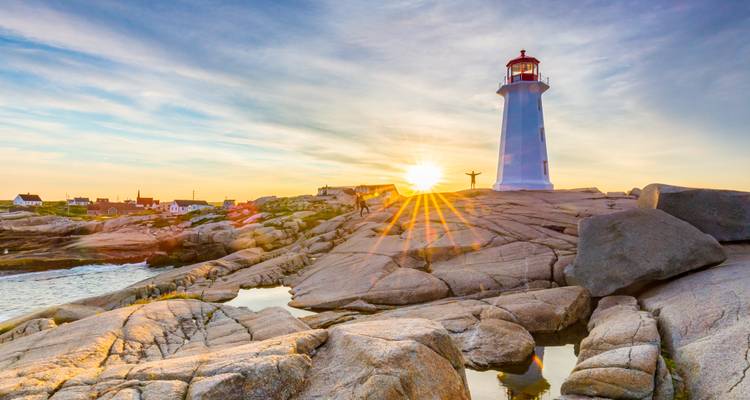 Iconic lighthouse on granite rocks with sunburst at golden hour near Peggy's Cove.