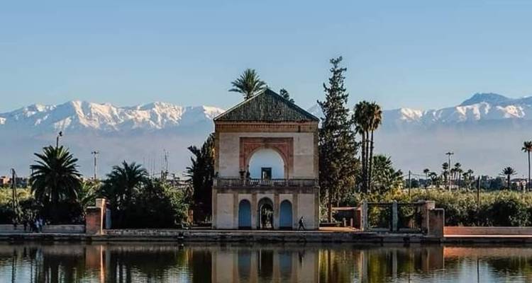 Reflecting pool with Menara pavilion backed by snow-capped Atlas Mountains under clear sky