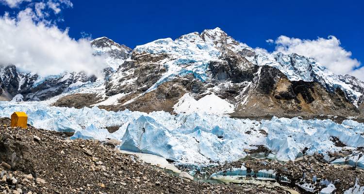 Wijd uitzicht op ijsblokken en besneeuwde bergkammen bij Everest Base Camp onder een strakblauwe hemel.