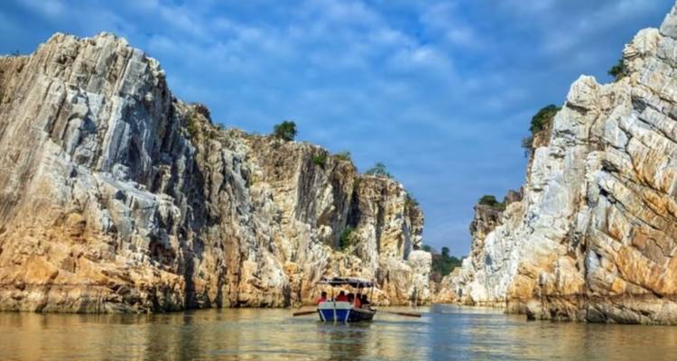 Boat cruising through towering marble cliffs on a calm river under a blue sky.