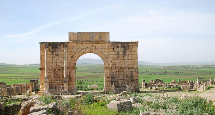 Oude Romeinse stenen boog te midden van groene velden op de archeologische site van Volubilis