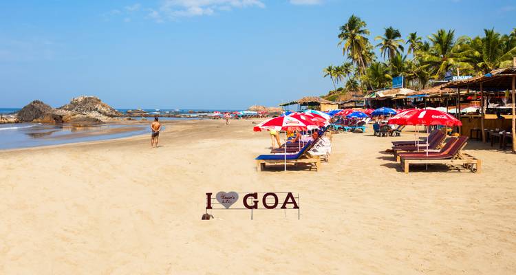 Sunny Goan beach with loungers, colorful umbrellas and a sign reading I love Goa, gentle waves in the background