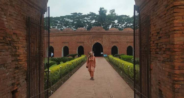 Visiteur encadré par une arche en brique marchant vers la cour de la mosquée historique aux Soixante Dômes
