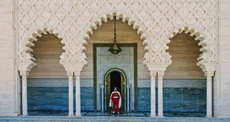 Koninklijke garde in rood uniform die onder sierlijke islamitische bogen staat bij de ingang van het Mausoleum in Rabat