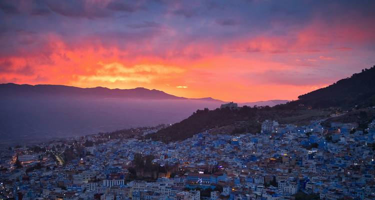 Stad Chefchaouen gloeiend blauw onder een levendige oranje zonsonderganghemel gezien van bovenaf
