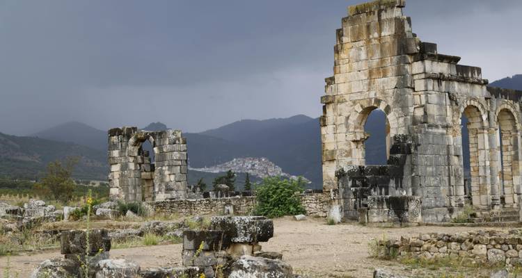 Donkere wolken hangen boven de stenen ruïnes van Volubilis met een verder weg gelegen heuveltstad in zicht.