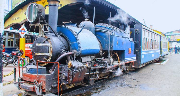 Blue steam locomotive of the famous Darjeeling Himalayan Railway emitting puffs of smoke at the station.