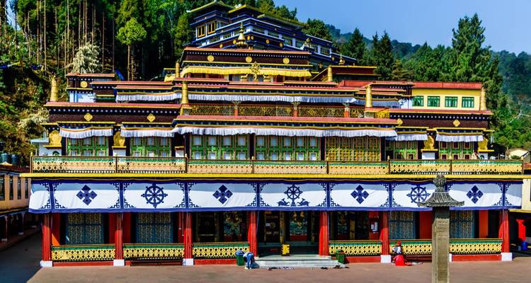Ornate multi-tiered monastery surrounded by tall trees under clear sky.