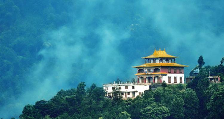 A solitary hilltop monastery emerges from swirling blue mist above a forested valley.