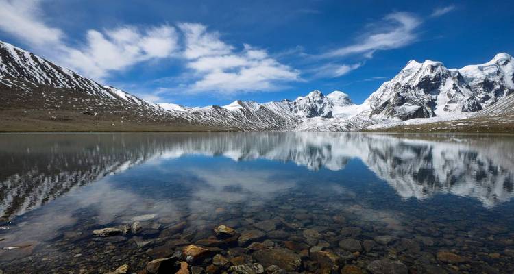 Crystal-clear alpine lake mirrors snow-clad peaks under a brilliant blue sky.
